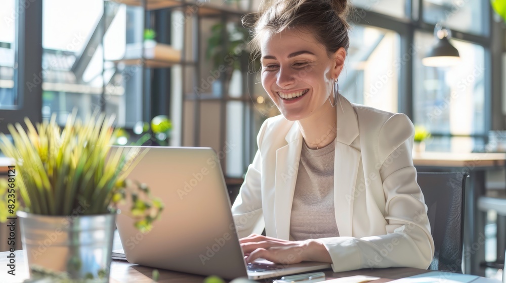 Smiling businesswoman working on a laptop in a modern office setting. Suitable for business blogs, corporate websites, and technology advertisements. Smiling businesswoman working on a laptop in a modern office setting. Suitable for business blogs, corporate websites, and technology advertisements.