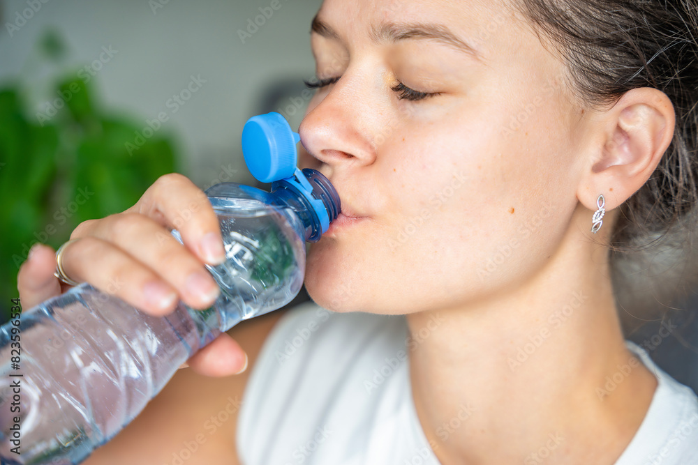 Young woman drinking from a bottle with stationary plastic cap. The new design means the cap remains attached to the bottle after opening, making the entire package easier to collect and recycle Young woman drinking from a bottle with stationary plastic cap. The new design means the cap remains attached to the bottle after opening, making the entire package easier to collect and recycle