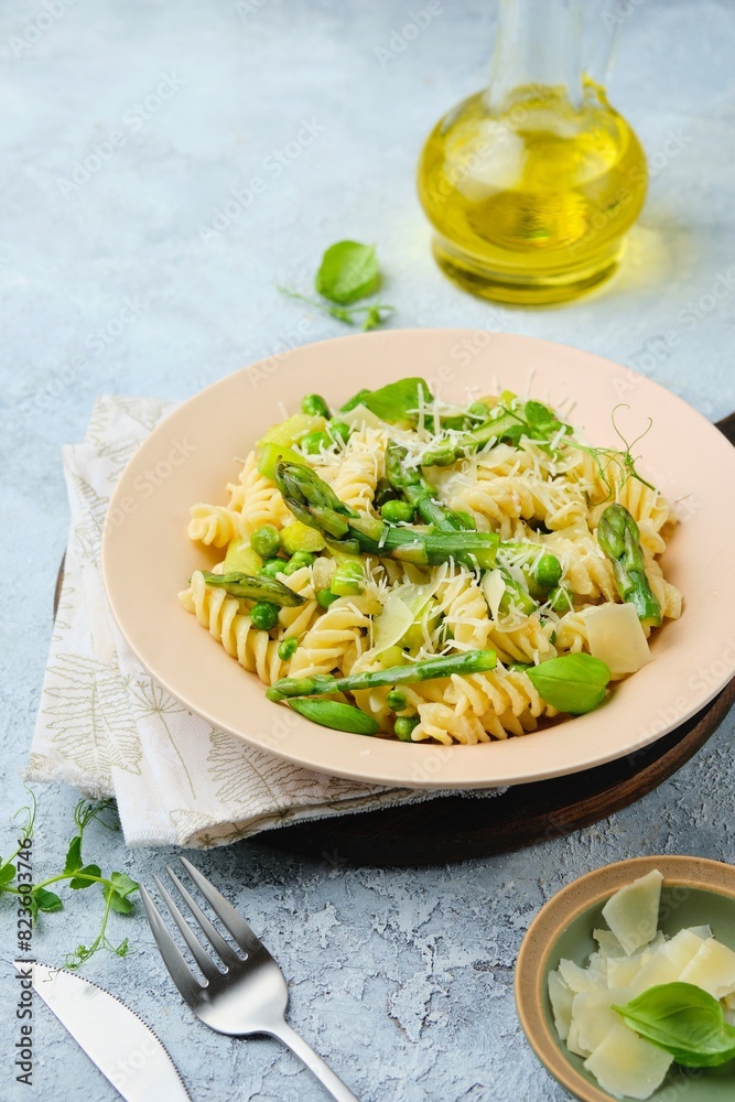 Pasta primavera, fusilli with green peas, asparagus and parmesan cheese in a ceramic plate on a gray concrete background. Asparagus recipes. Italian Cuisine. Pasta primavera, fusilli with green peas, asparagus and parmesan cheese in a ceramic plate on a gray concrete background. Asparagus recipes. Italian Cuisine.