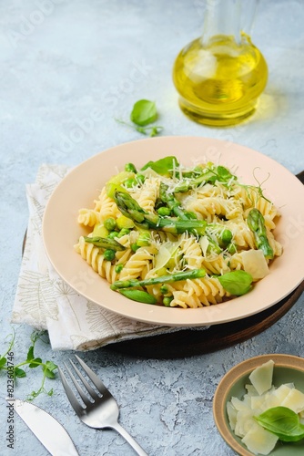 Pasta primavera, fusilli with green peas, asparagus and parmesan cheese in a ceramic plate on a gray concrete background. Asparagus recipes. Italian Cuisine.