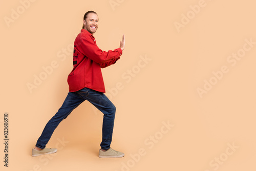 Full size profile photo of nice young man arms push empty space wear red shirt isolated on beige color background © deagreez