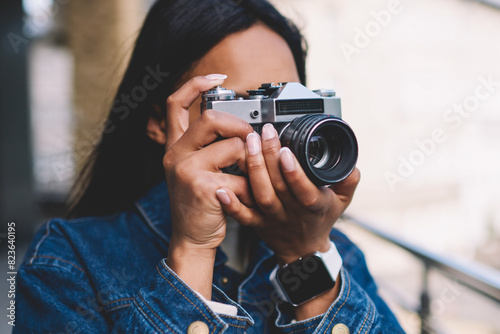 Young dark skinned hipster girl in jeans jacket spending time on hobby taking pictures on city street while resting on weekends,afro american tourist making photos during leisure strolling outdoors #823640195