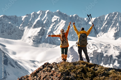 Two happy active hikers are standing in winner pose with open arms against glacier and mountain