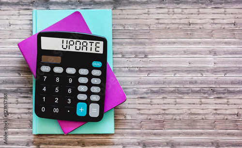 calculator with the word UPDATE on display with notepads on a wooden background. Business