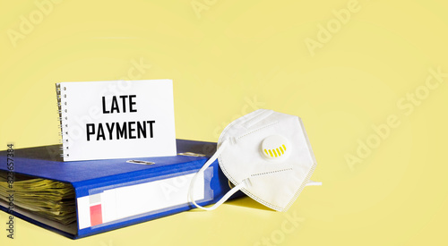 Medical mask, folder and notepad with the text LATE PAYMENT on a yellow background.