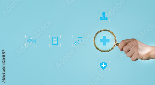 Hand holding a magnifying glass over a plus sign on a blue background. copy space health insurance concept