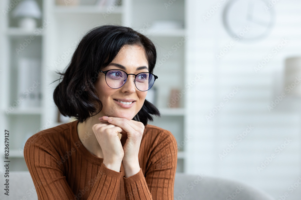 Smiling woman with glasses sitting indoors in a cozy home environment Smiling woman with glasses sitting indoors in a cozy home environment