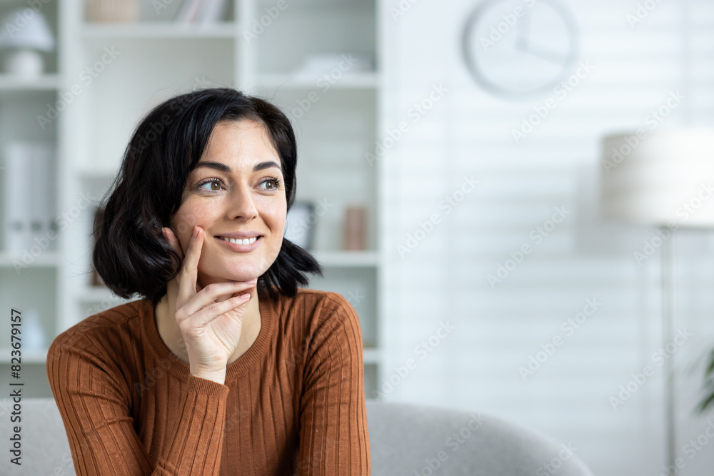 Smiling woman in casual attire thinking while sitting in modern living room Smiling woman in casual attire thinking while sitting in modern living room