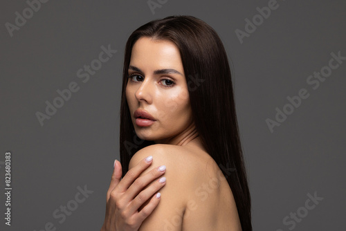 Portrait of woman with natural nude make up with bare shoulders on gray background.