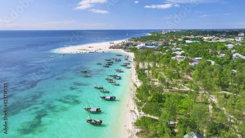 Aerial view of the boats on tropical sea coast with white sandy beach on summer sunny day. Travel in Kendwa, Zanzibar island. Landscape with boats, clear blue water, sky, clouds, palms. Top drone view