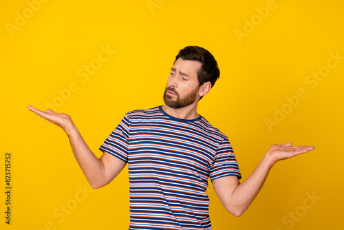 Photo of minded man dressed striped t-shirt directing look at best variant on palm empty space isolated on yellow color background photo