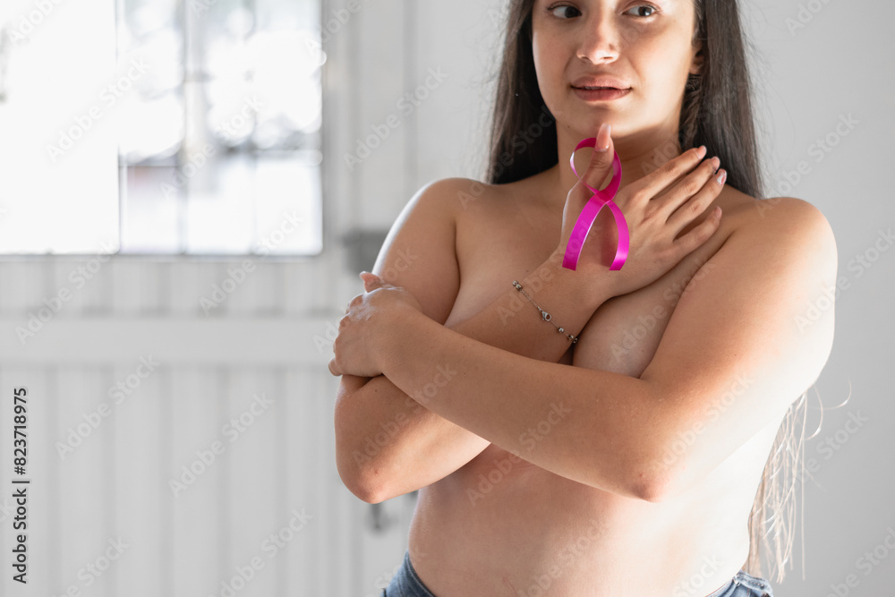 © Mauricio Toro - latina woman covering her breasts with her hands while holding a pink ribbon. fight against cancer