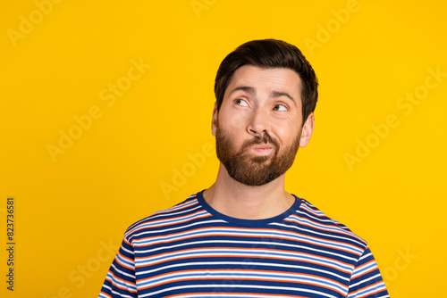 Portrait of smart suspicious guy with stylish stubble wear striped t-shirt look at offer empty space isolated on yellow color background
