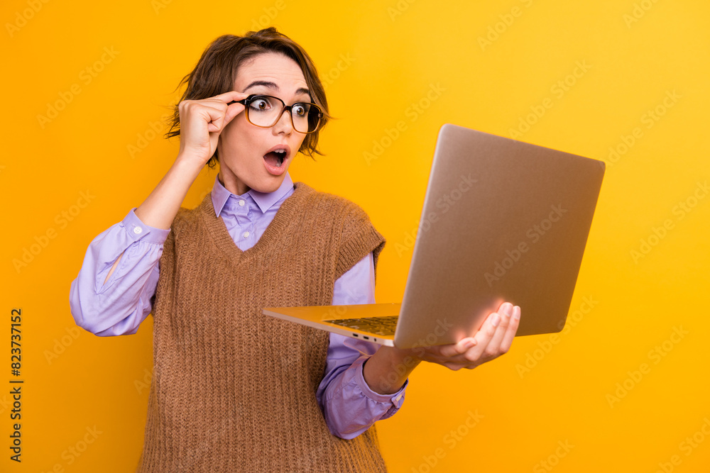 Portrait of charming woman with bob hairdo wear knit waistcoat touch glasses staring at laptop isolated on yellow color background Portrait of charming woman with bob hairdo wear knit waistcoat touch glasses staring at laptop isolated on yellow color background