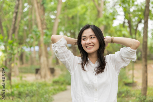 Portrait of asian woman breathing fresh air in a forest.Carefree asian girl smiling and enjoying summer sunny day in park.Young woman arms raised enjoying the fresh air in green park.