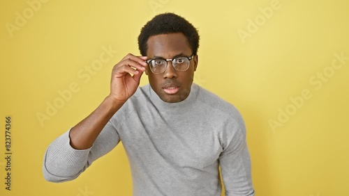 Scared and amazed! young african american man, glasses-wearing, agape with disbelief over isolated yellow background photo