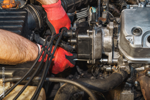 The mechanic is reassembling the distributor.  Replacing a rubber gasket. Valve cover, air filter intake pipe, ignition coil.