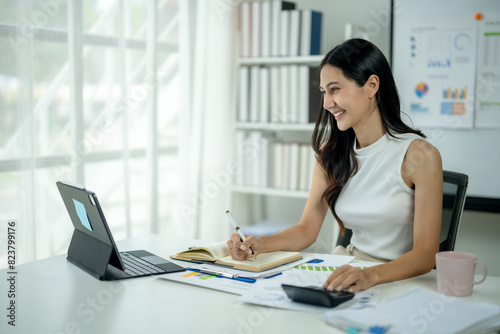 A woman is sitting at a desk with a laptop and a notebook © Wasana