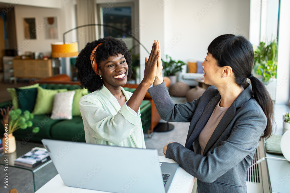 Two professional women celebrating success with a high-five in a stylish office Two professional women celebrating success with a high-five in a stylish office