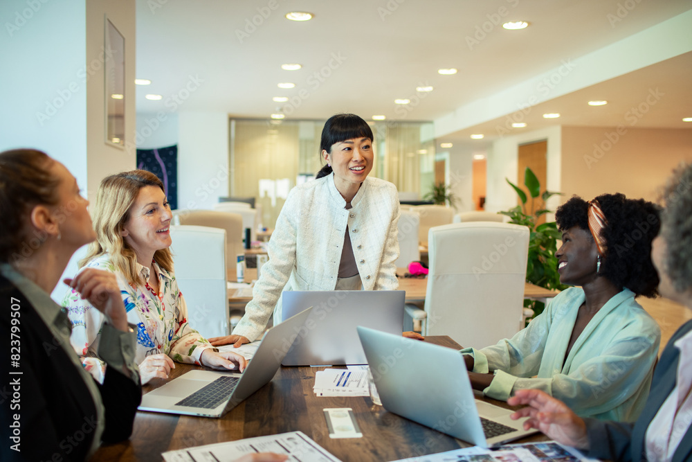 © Marko Geber - Multiethnic female colleagues discussing work with laptops in a modern office