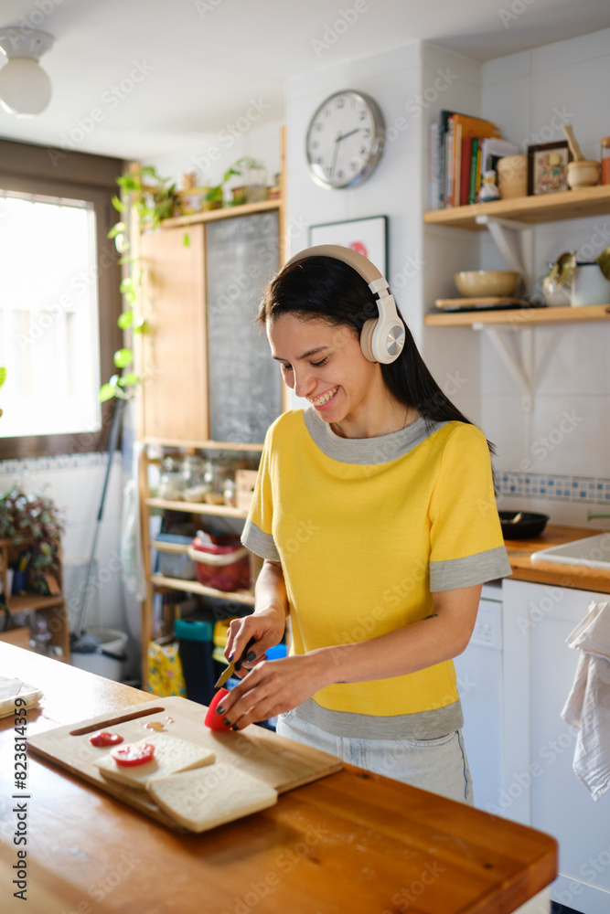 Smiling Woman in the kitchen making a sandwich using headphones Smiling Woman in the kitchen making a sandwich using headphones