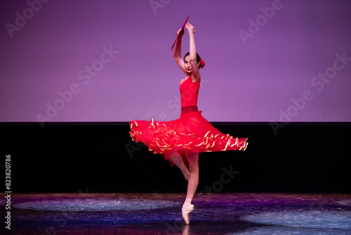 ballerina in a red dress performs a variation from the ballet Don Quixote on the theater stage.