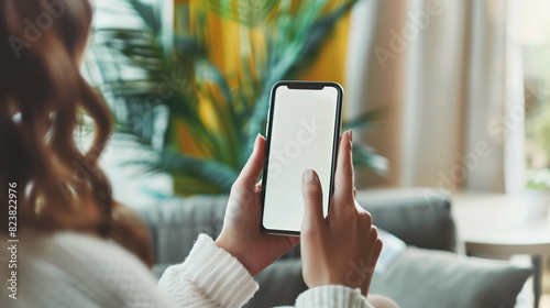 Young woman hands holding cell phone touching finger on mockup white blank display, empty screen for social media app ad at home. Mobile application tech concept, over shoulder view. Generative AI.
