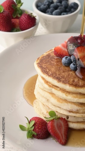 pouring syrup on piled pancake with strawberries and bluberries