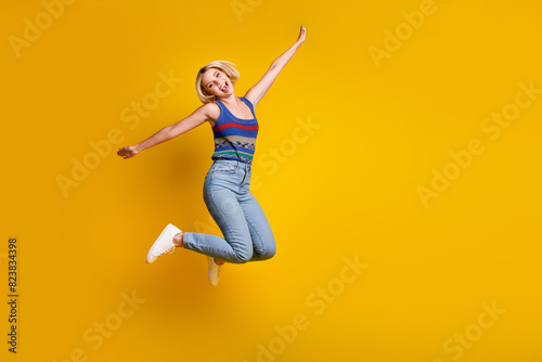 Full body length photo of sportive funny jumping woman enjoying warm spring days flying like a bird isolated on yellow color background