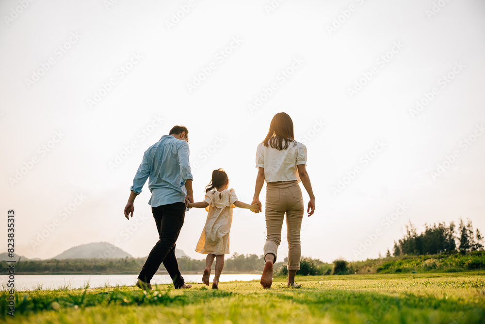 Happy Asian family walking and playing together in a beautiful nature setting, with green grass and a sunny background, on a summer day, Family day, back view Happy Asian family walking and playing together in a beautiful nature setting, with green grass and a sunny background, on a summer day, Family day, back view