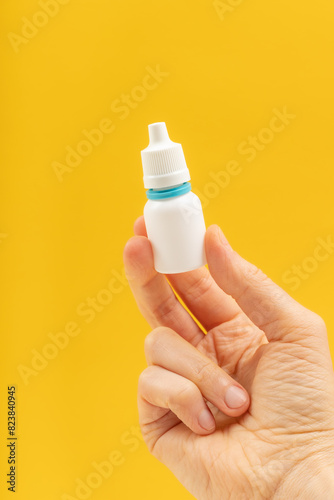 A hand is holding a white plastic medical bottle with a white and blue cap