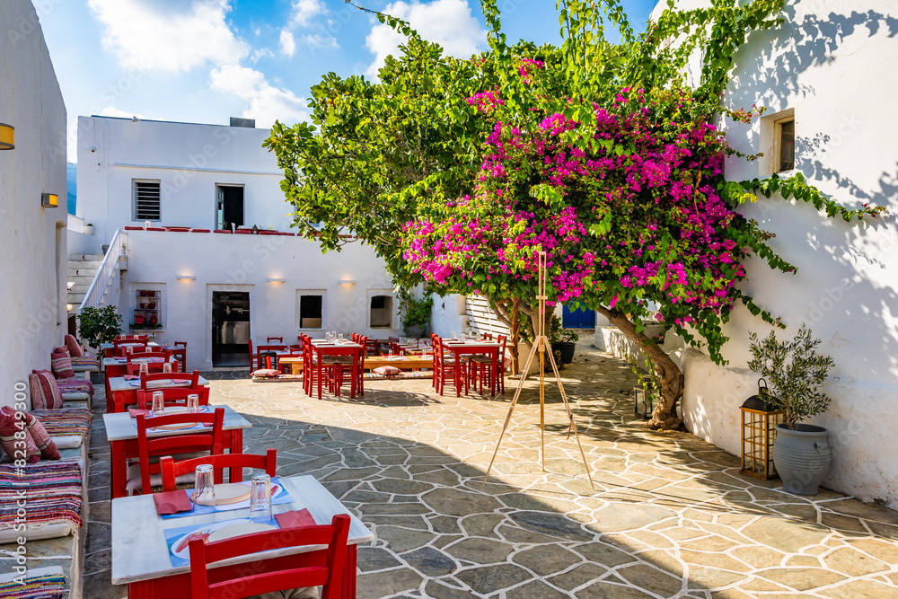 Typical Greek taverna restaurant with red chairs and bougainvillea flowers on square in Apollonia village, Sifnos island, Greece