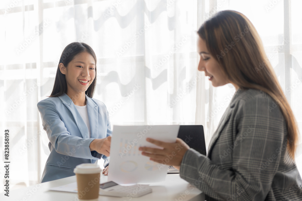 Two young Asian businesswomen work on laptop computers in the office with reports. Colleagues discuss financial data in document analysis of new marketing projects. Two young Asian businesswomen work on laptop computers in the office with reports. Colleagues discuss financial data in document analysis of new marketing projects.