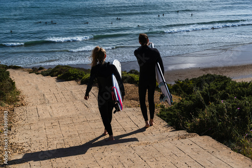Surfers descending the steps of Praia do Beliche beach in Sagres, Algarve, Portugal. Sunny day with surfers in the sea. Boy and girl photo