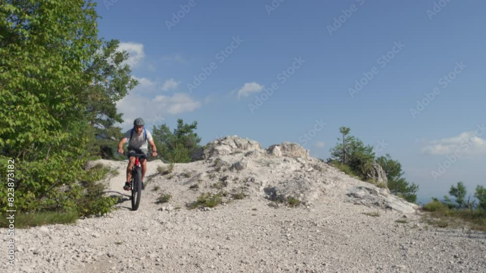 Slow motion of a male electric mountain bike rider going downhill and braking on a hilly rocky trail, low-angle shot. E-mountain biking concept. Slow motion of a male electric mountain bike rider going downhill and braking on a hilly rocky trail, low-angle shot. E-mountain biking concept.