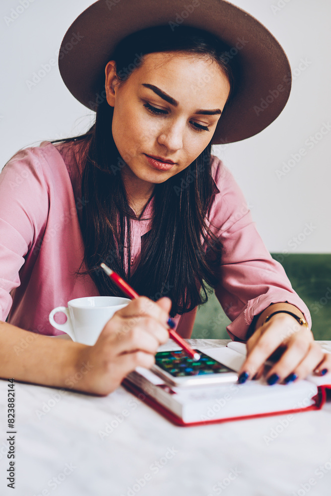 Pensive young woman in trendy hat installing application on smartphone for organizing day sitting in cafe,female student texting message on mobile phone chatting in social network during break Pensive young woman in trendy hat installing application on smartphone for organizing day sitting in cafe,female student texting message on mobile phone chatting in social network during break