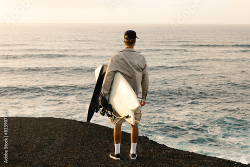 A man surveys the ocean waves while grasping a twinfin surfboard photo