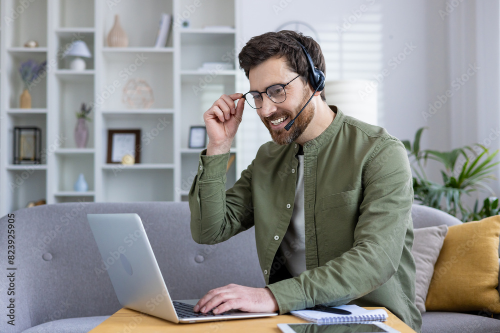 Confident man working from home using a laptop and headset, smiling pleasantly. Home office setup with a cozy background. Concept of remote work and online communication. Confident man working from home using a laptop and headset, smiling pleasantly. Home office setup with a cozy background. Concept of remote work and online communication.