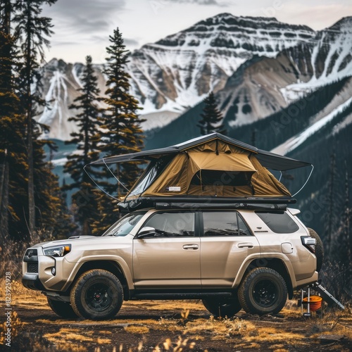 A tan SUV with a roof top is parked on a grassy hillside next to a mountain photo