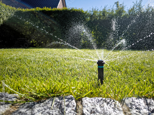 A sprinkler is watering a wellkept green lawn under the sky