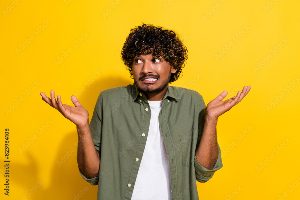 Portrait of young hispanic guy in khaki shirt indifferent shrug shoulders misunderstanding look mockup isolated on yellow color background