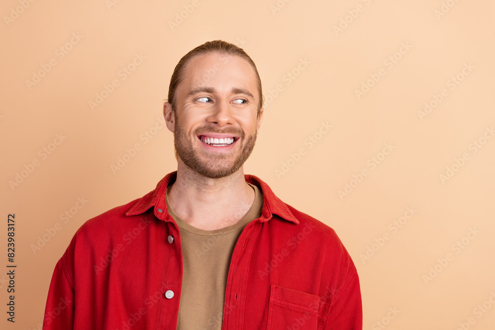 Photo of nice young man look empty space wear red shirt isolated on beige color background Photo of nice young man look empty space wear red shirt isolated on beige color background
