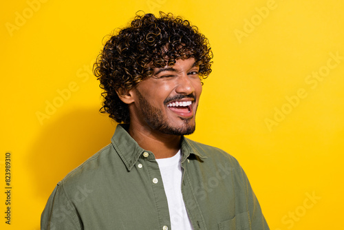 Portrait photo of young attractive hispanic guy in khaki shirt blinking eye and flirting with you isolated on yellow color background