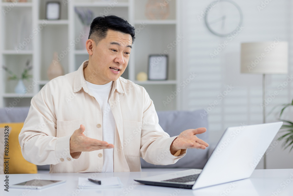 Man in casual wear gesturing while having an online meeting on a laptop at home. Modern interior and communication concept. Man in casual wear gesturing while having an online meeting on a laptop at home. Modern interior and communication concept.