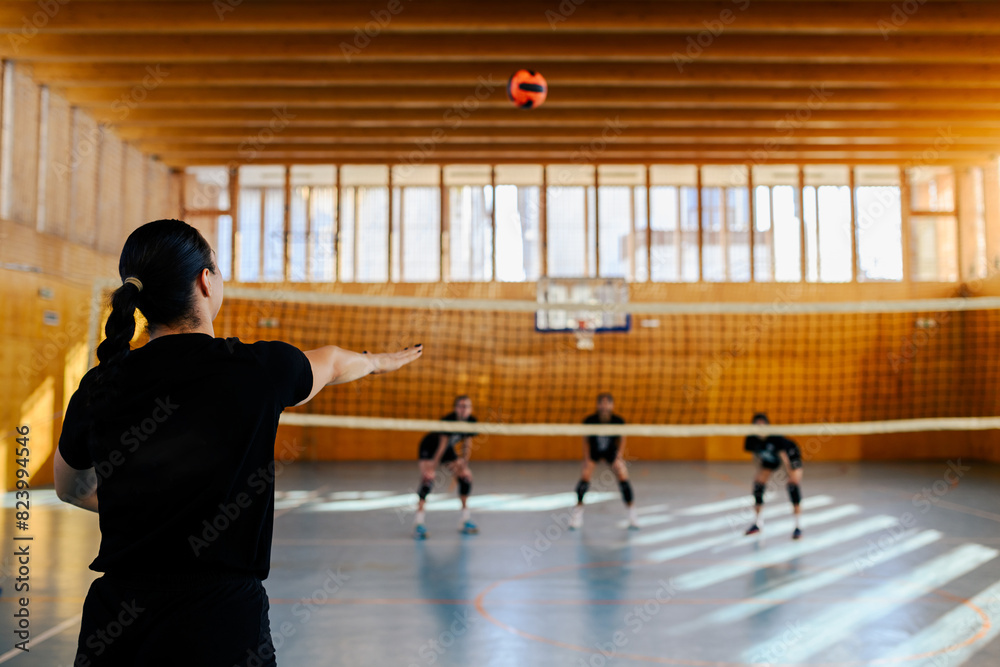 Rear view of a female volleyball player serving the ball in a sports hall Rear view of a female volleyball player serving the ball in a sports hall