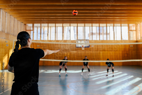Rear view of a female volleyball player serving the ball in a sports hall