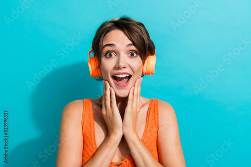 Photo of impressed woman dressed knitwear singlet in headphones astonished staring palms on cheeks isolated on turquoise color background photo