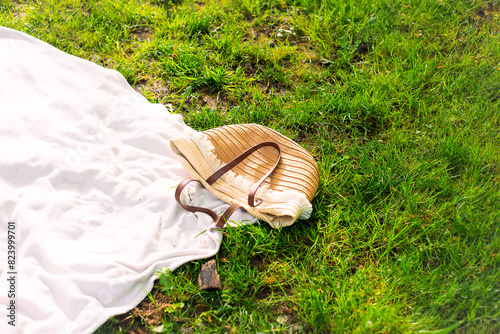 A wicker bag rests on a white blanket amidst grass in a natural landscape