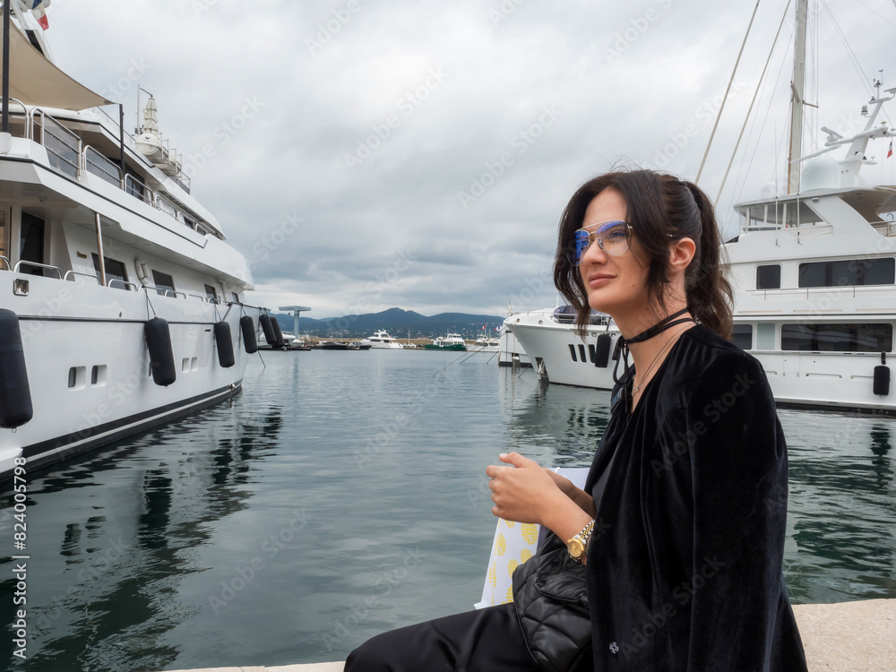 Beautiful young woman in a chic dress poses elegantly near moored yachts Beautiful young woman in a chic dress poses elegantly near moored yachts