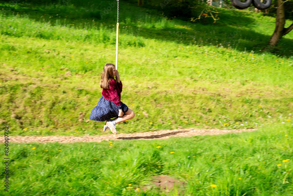 Person leisurely swinging on a yellow rope by trees on a dirt path